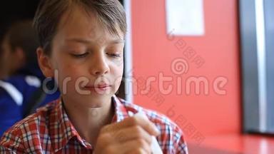 一个男孩正在咖啡馆里吃冰淇淋。 咖啡馆里那个金发男孩正在用勺子吃冰淇淋。